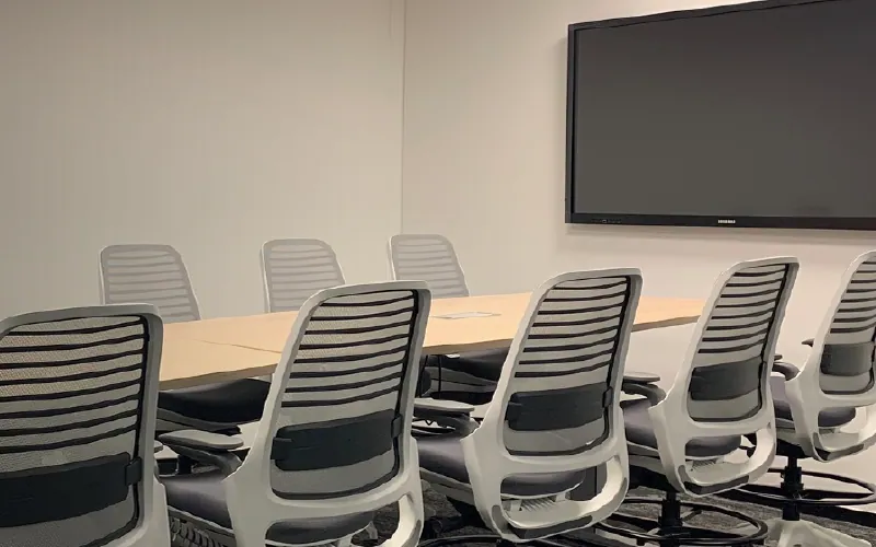 Sala de reuniones con mesa de directorio y pantalla